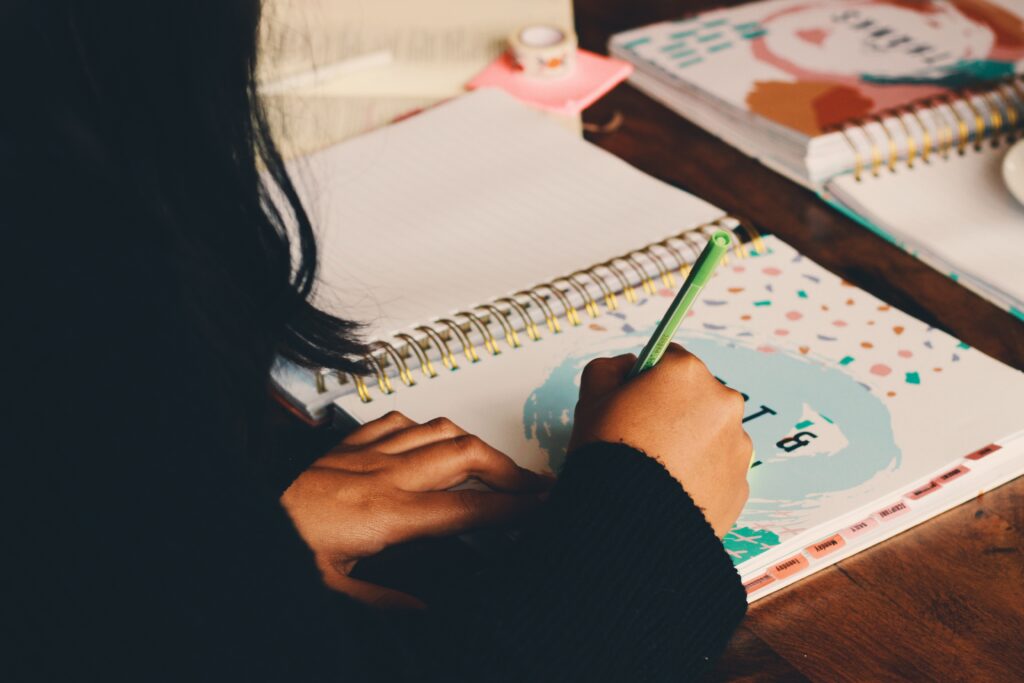 Woman seated at a table, writing in her prayer journal with a pen.