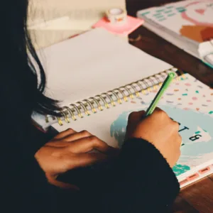 Woman seated at a table, writing in her prayer journal with a pen.