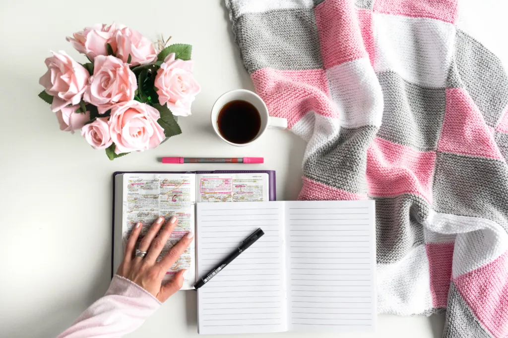 Bible Study Academy: Girl with her Devotional Bible study. Woman's hand is turning a page of the Bible. With pink roses, black tea and coffee.